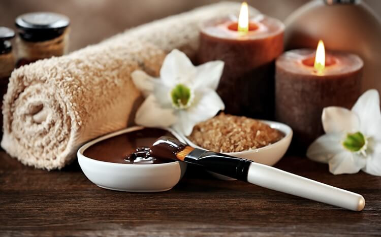 miseczka i szpatułka z płynną czekoladą na tle ręcznika, białych kwiatów i świec zapachowych